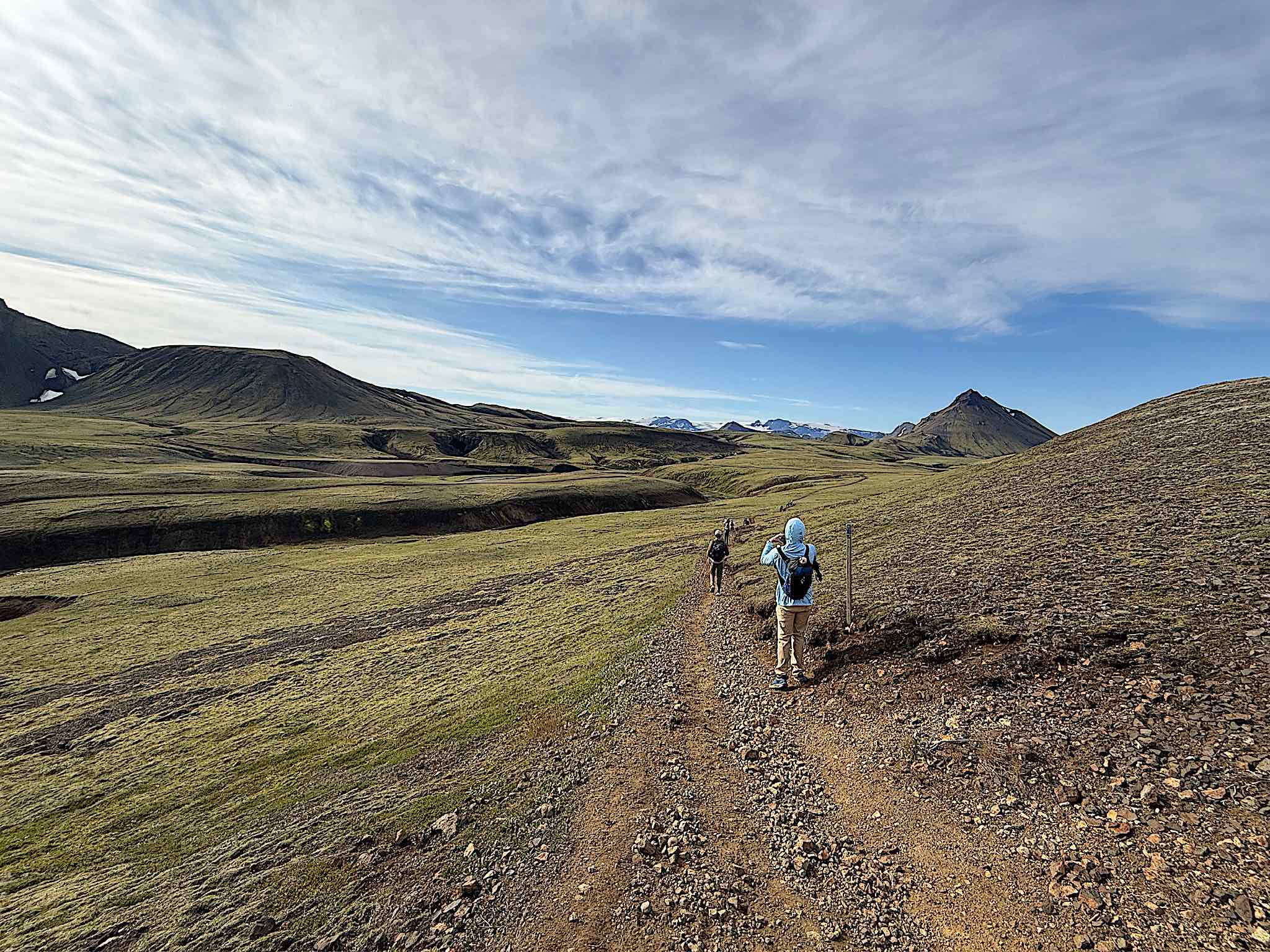 Hikers strung out along the trail in the green Highlands under a wide sky