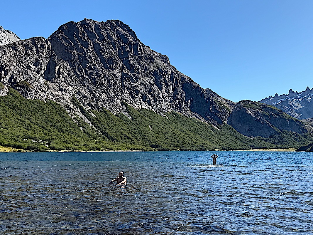Two people swimming in a cold alpine lake beneath a granite wall in the Nahuel Huapi range