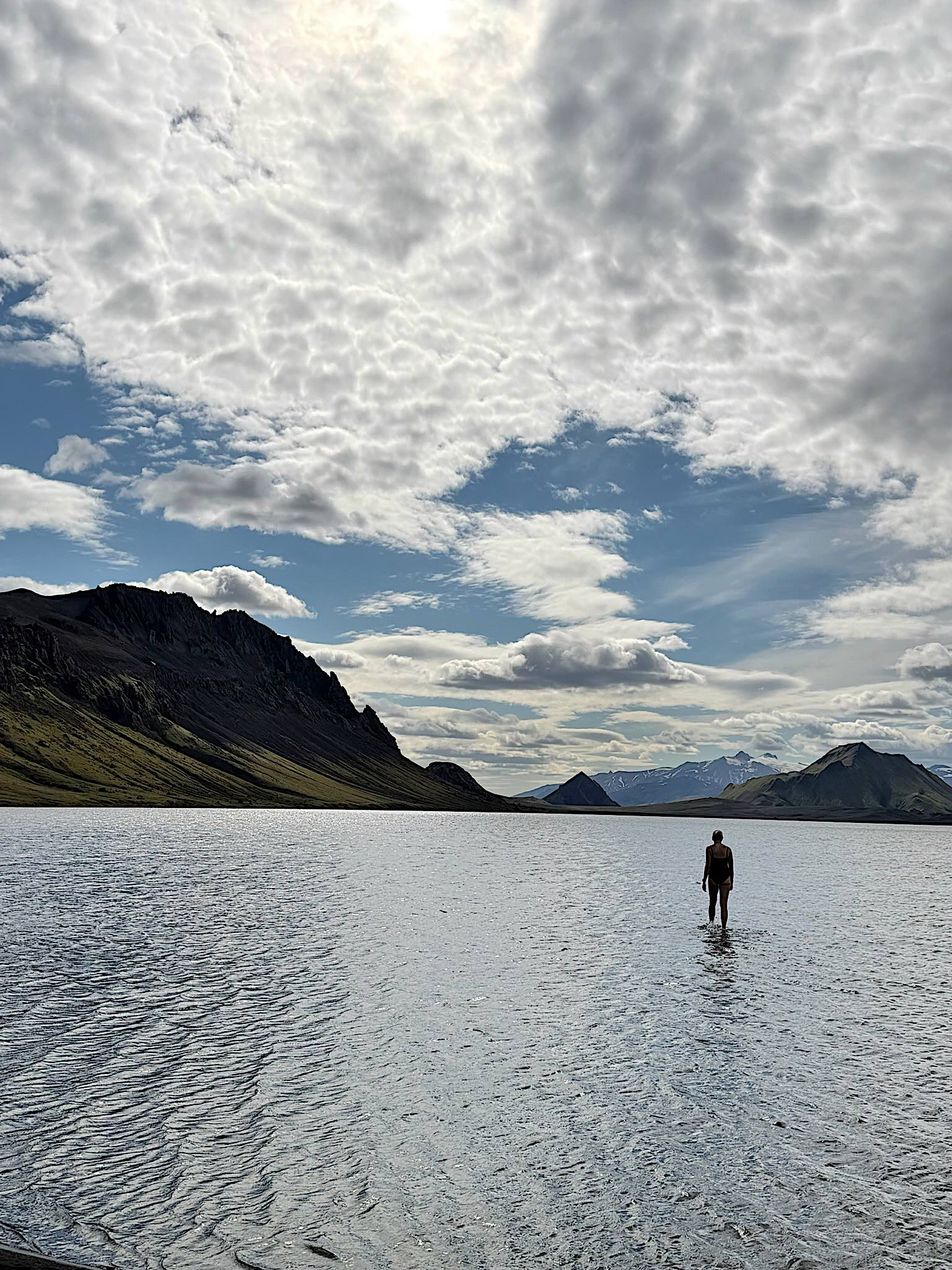 A swimmer walking into the lake at Alftavatn under a mackerel sky