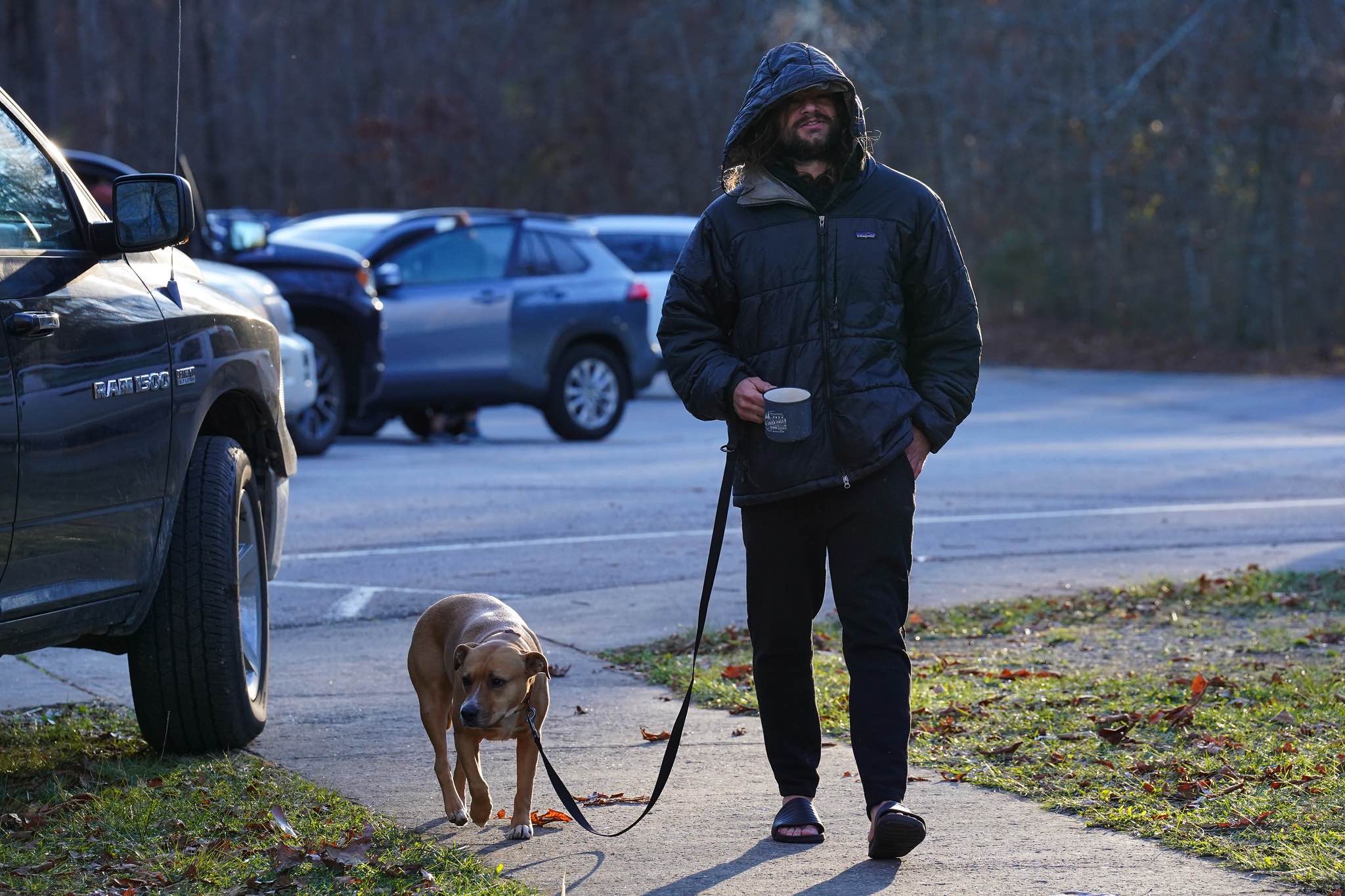 A bundled participant walks a dog with a hot drink on a cold morning