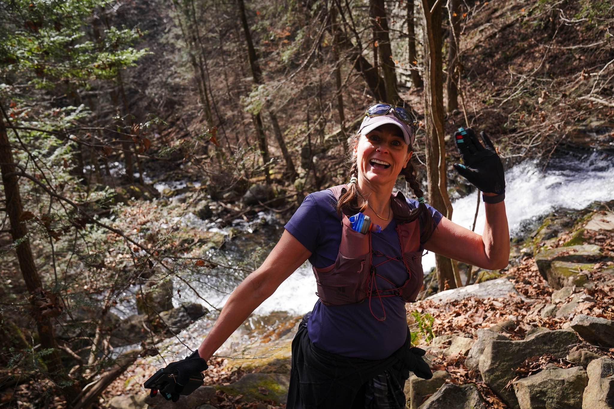 A smiling runner waves beside a waterfall on the Fiery Gizzard course