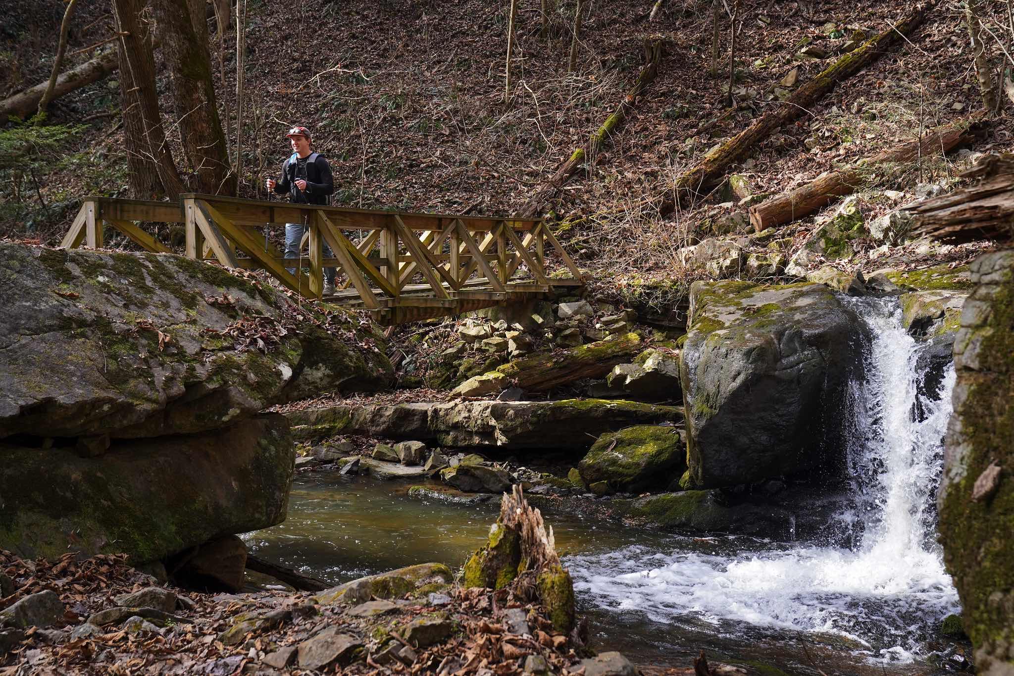 A runner crosses a wooden footbridge beside a small waterfall