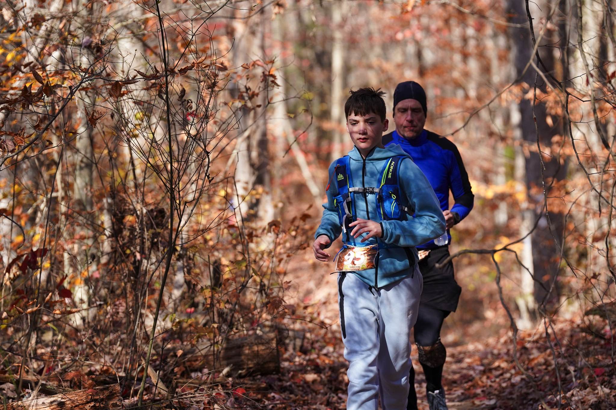 A young runner leads an adult along a sunlit autumn trail